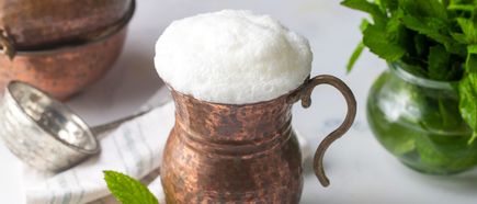 Ayran in kupfernem Becher mit dichtem Schaum, daneben frische Minze und traditionelles Serviergeschirr