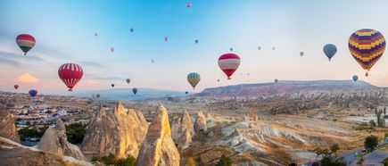 Heißluftballons über den Felsformationen Kappadokiens bei Sonnenaufgang, weite Landschaft mit Tuffkegeln und Tälern in der Türkei
