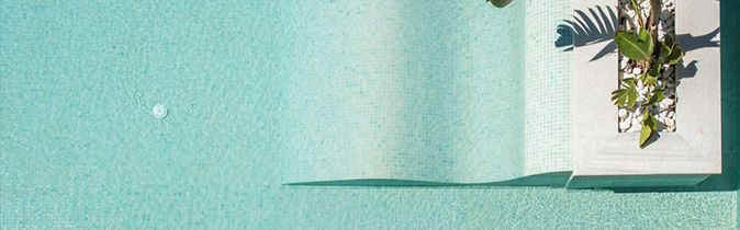 Vogelperspektive auf einen rechteckigen Pool mit zwei weißen Stühlen und einem runden Tisch auf einer Holzterrasse sowie zwei Pflanzen in Töpfen