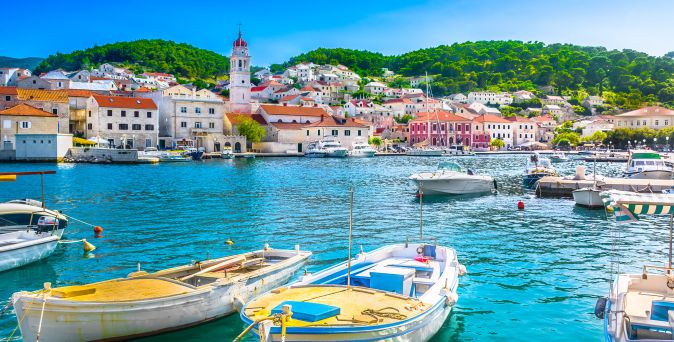 Hafenansicht von Pučišća auf der Insel Brač in Kroatien mit traditionellen Natursteinhäusern, Kirchturm und festgemachten Booten am Wasser