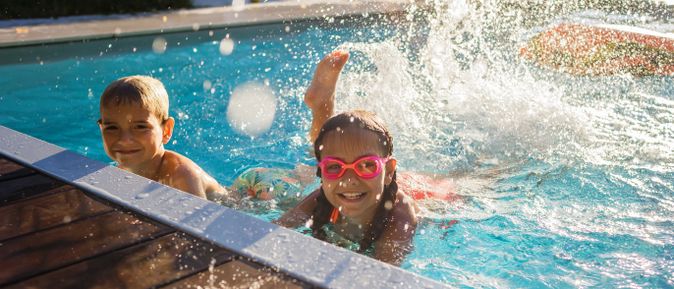 Kinder spielen in einem Außenpool und planschen im Wasser, während Wasserspritzer und sommerliches Badevergnügen einen familienfreundlichen Urlaub mit Pool zeigen