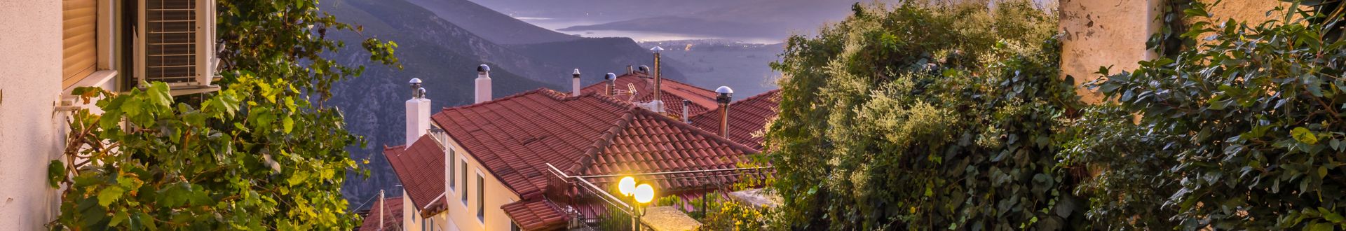 Blick auf ein Dorf mit roten Ziegeldächern und gepflastertem Weg in den Bergen der Peloponnes bei Sonnenuntergang