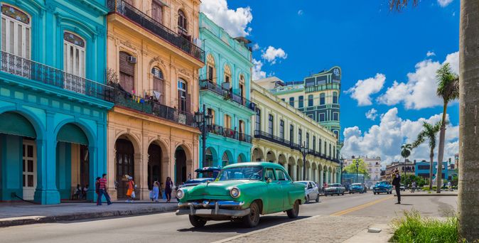Grünes Oldtimer-Auto fährt an bunten Kolonialgebäuden auf einer Straße in Kuba vorbei