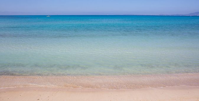 Strandansicht auf Mallorca mit klarem, türkisfarbenem Wasser und sanften Wellen, die auf den hellen Sand treffen.