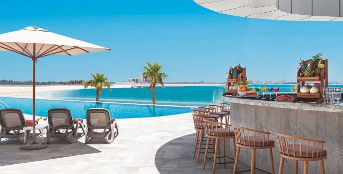 Poolbereich mit Liegestühlen und Sonnenschirm, Bar mit tropischen Getränken und Obst, Blick auf Meer und Palmen