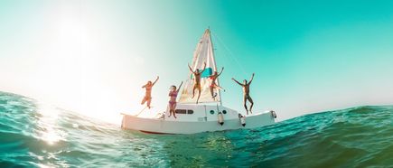 Gruppe von Menschen springt fröhlich von einem Segelboot ins Meer
