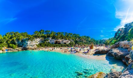 Strand Cala Llombards auf Mallorca mit kristallklarem Wasser, hellem Sandstrand, Badegästen und felsiger Küstenlandschaft unter blauem Himmel