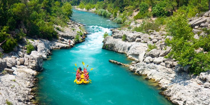 Rafting-Gruppe im gelben Schlauchboot auf türkisblauem Fluss in einer felsigen Schlucht, umgeben von grünen Bäumen
