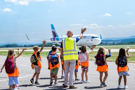 Flughafenführung für Kinder am Flughafen Stuttgart mit Blick auf ein Passagierflugzeug auf dem Vorfeld und einer begleiteten Besuchergruppe in Sicherheitswesten