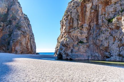 Eingang zur Schlucht Torrent de Pareis auf Mallorca mit hohen, steilen Felswänden, hellem Kiesstrand und Blick auf das blaue Meer
