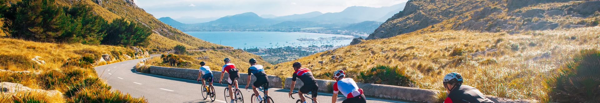 Gruppe von fünf Radfahrern auf einer kurvigen Bergstraße mit Blick auf die Küste und das blaue Meer bei Sonnenschein