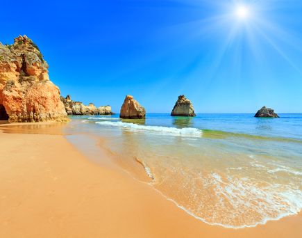Algarve-Küste mit goldfarbenen Felsen, ruhigem Meer und hellem, sonnigem Himmel.