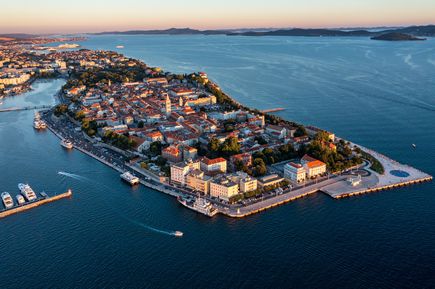 Luftaufnahme der Altstadt von Zadar in Kroatien mit historischen Gebäuden, Hafenanlagen, Booten und Promenade, umgeben vom tiefblauen Wasser der Adria