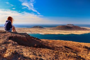 Aussicht vom Mirador del Río auf Lanzarote mit Blick über die vulkanische Landschaft und den Atlantik, eine sitzende Person auf einer Felskante im Vordergrund