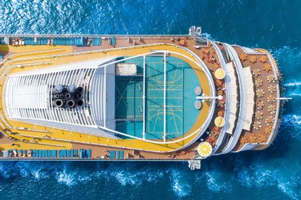 Luftaufnahme des oberen Decks eines großen Kreuzfahrtschiffs mit Sportplatz, Sonnendeck und Sitzbereichen, umgeben von tiefblauem Meer