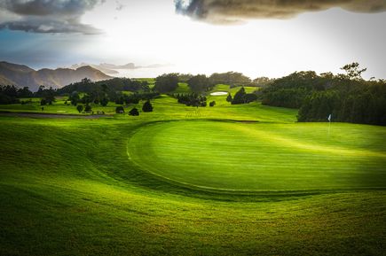 Weitläufiger Golfplatz Santo da Serra auf Madeira mit gepflegtem Grün, Fahne auf dem Putting Green und bewaldeter Hügellandschaft im Hintergrund