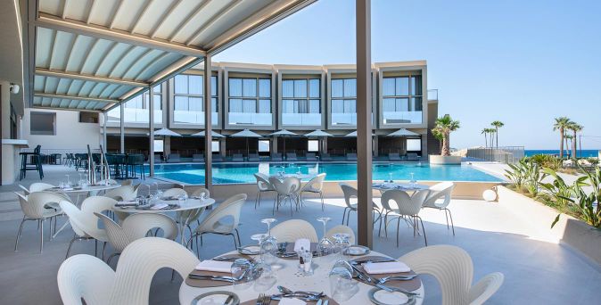 Freiluftrestaurant mit gedeckten Tischen und Stühlen neben einem Pool unter einem modernen Sonnendach mit Blick auf das Meer