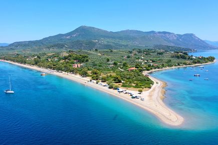 Luftaufnahme einer schmalen Landzunge mit Sandstrand, umgeben von blauem Meer und bewaldeten Hügeln im Hintergrund