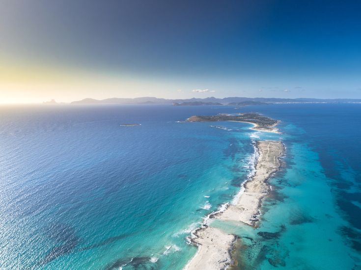 Ses Illetes auf Formentera aus der Luft mit schmaler Sandzunge, türkisfarbenem Meer auf beiden Seiten, flachem Küstenverlauf und Inseln am Horizont