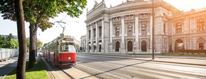 Roter Straßenbahnzug fährt vor dem historischen Burgtheater in Wien