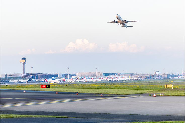 Flugzeug im Steigflug über Start- und Landebahn mit Terminalgebäuden und mehreren geparkten Flugzeugen im Hintergrund am Flughafen Düsseldorf
