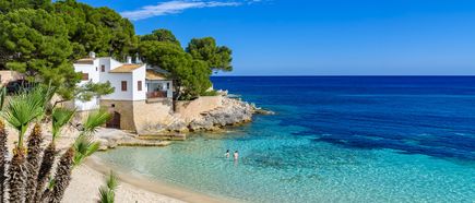 Kleine Sandbucht mit klarem Wasser in Cala Ratjada auf Mallorca, gesäumt von Felsen, Pinien und einem weißen Haus