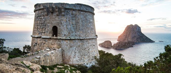 Alter Wachturm Torre d’es Savinar auf Ibiza mit Blick auf die Felseninsel Es Vedrà im Sonnenuntergang