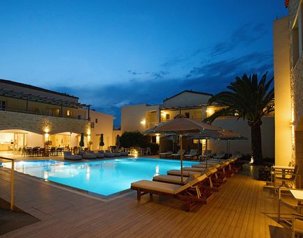 Beleuchteter Außenpool mit Liegen und Sonnenschirmen vor einem mehrstöckigen Hotelgebäude bei Abenddämmerung