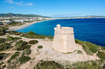 Luftaufnahme der Playa d’en Bossa auf Ibiza mit langem Sandstrand, blauem Meer und historischem Wehrturm im Vordergrund