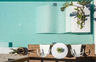 Vogelperspektive auf einen rechteckigen Pool mit zwei weißen Stühlen und einem runden Tisch auf einer Holzterrasse sowie zwei Pflanzen in Töpfen