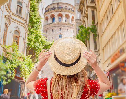 Person mit Strohhut steht in einer belebten Straße und blickt auf den historischen Galataturm in Istanbul