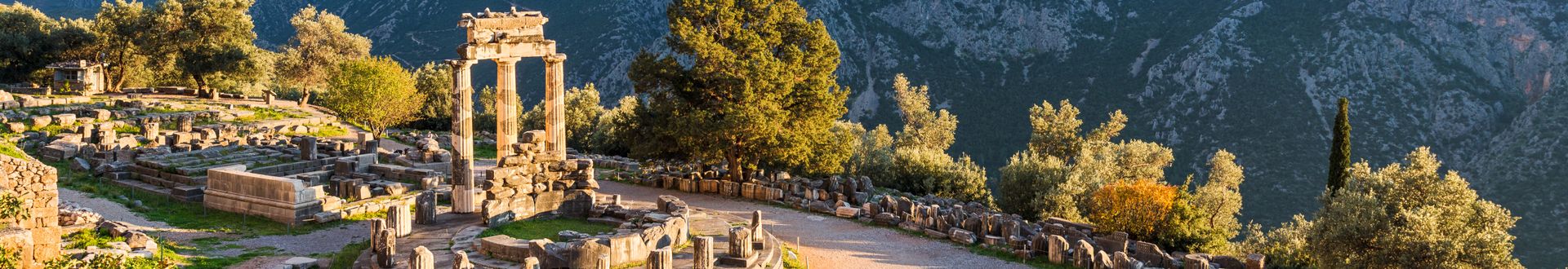 Ruinen einer antiken Tempelanlage in einer bergigen Landschaft mit Bäumen und blauem Himmel.