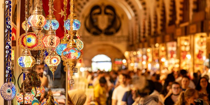 Bunt leuchtende orientalische Lampen und Nazar-Amulette in einem Geschäft des Gewürzbasars in Istanbul, mit belebten Gängen und vielen Besuchern im Hintergrund