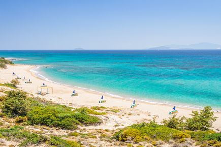 Langer Sandstrand mit vereinzelten Sonnenschirmen und türkisfarbenem Meer an der Küste von Kos