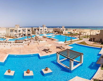Blick auf das True Beach Village in Ägypten mit mehreren Pools und niedrigen Gebäuden mit dem Meer im Hintergrund.