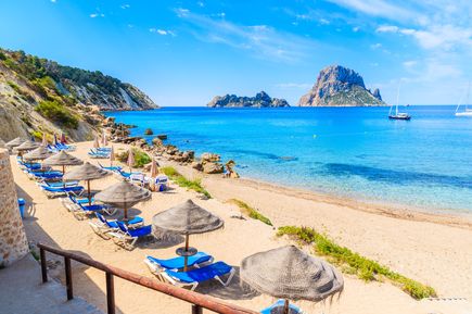 Strand Cala d’Hort auf Ibiza mit Liegen und Sonnenschirmen, Blick auf die Insel Es Vedrà im Hintergrund