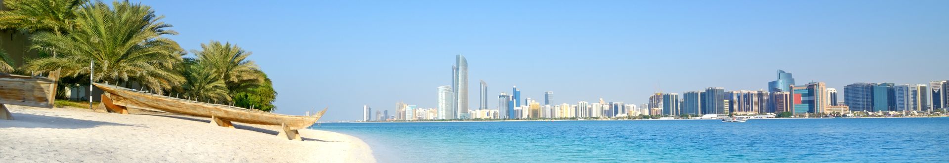 Blick auf die Skyline von Abu Dhabi mit modernen Gebäuden, Palmen am Strand und klarem Wasser im Vordergrund.