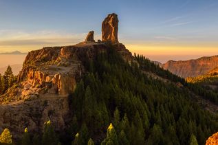 Felsformation Roque Nublo auf Gran Canaria bei warmem Abendlicht, über einem bewaldeten Hochplateau mit Blick auf die umliegende Vulkanlandschaft der Insel