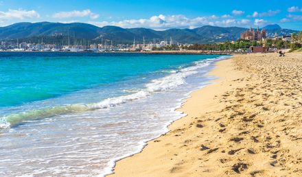 Weitläufiger Strand Playa de Palma auf Mallorca mit sanften Wellen, Blick auf die Kathedrale von Palma und die umliegenden Berge