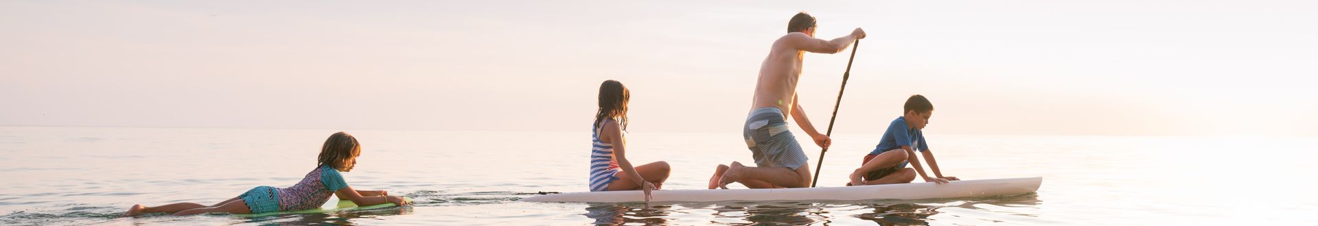 Familie beim Stand-up-Paddling auf ruhigem Meer während eines sonnigen Urlaubstags.