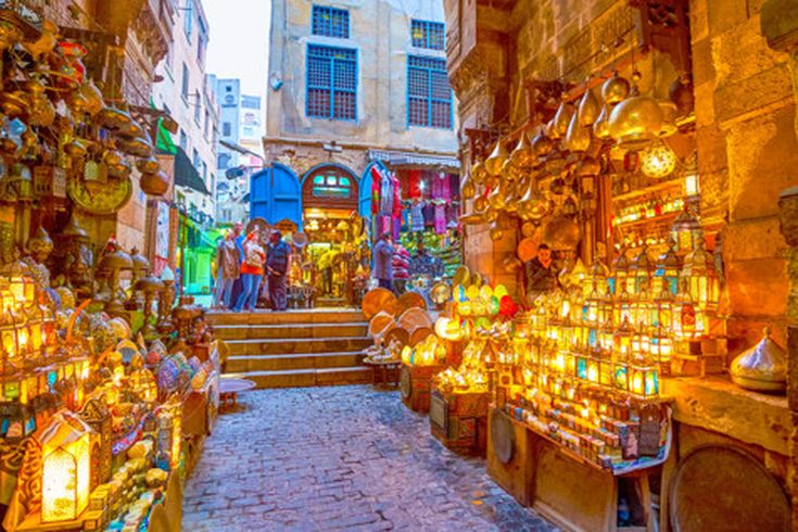 Belebter Markt Khan al-Khalili in Kairo mit Ständen, die Kupferwaren und Lampen verkaufen, gepflasterter Straße und historischen Gebäuden
