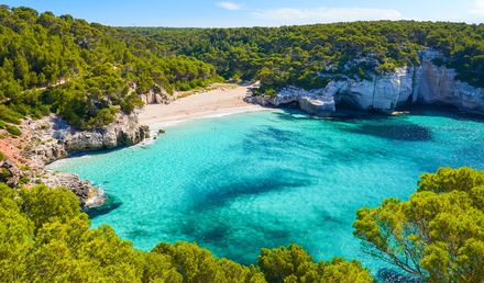 Idyllische Bucht Cala Mitjaneta auf Menorca mit weißem Sandstrand, türkisfarbenem Wasser und von Klippen umgeben
