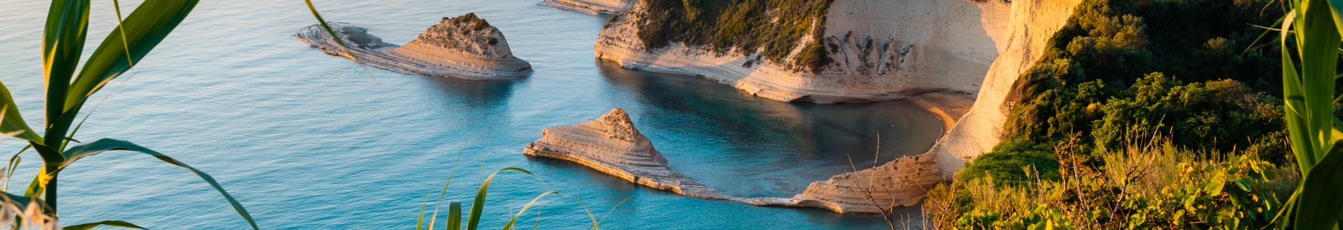 Felsige Küstenformationen mit steilen Klippen und kleinen Buchten am Kap Drastis auf Korfu vor ruhigem Meer und klarem Himmel