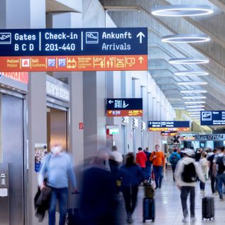 Passagiere mit Rollkoffern im Terminal des Flughafens Köln/Bonn unter gut sichtbaren Wegweisern zu Gates, Check-in-Bereichen und Ankunft