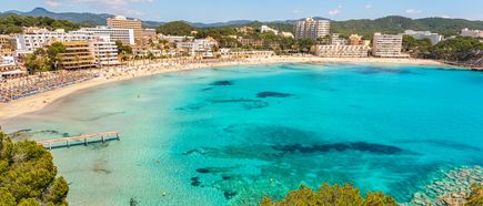 Blick auf den Strand von Paguera auf Mallorca mit türkisblauem Wasser, zahlreichen Sonnenliegen und Hotels im Hintergrund