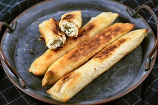 Goldbraune Börek-Rollen auf Blech, eine aufgeschnitten mit sichtbarer Käse-Kräuter-Füllung