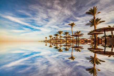 Spiegelglatter Pool mit Palmen und Sonnenschirmen unter bewölktem Himmel in Hurghada