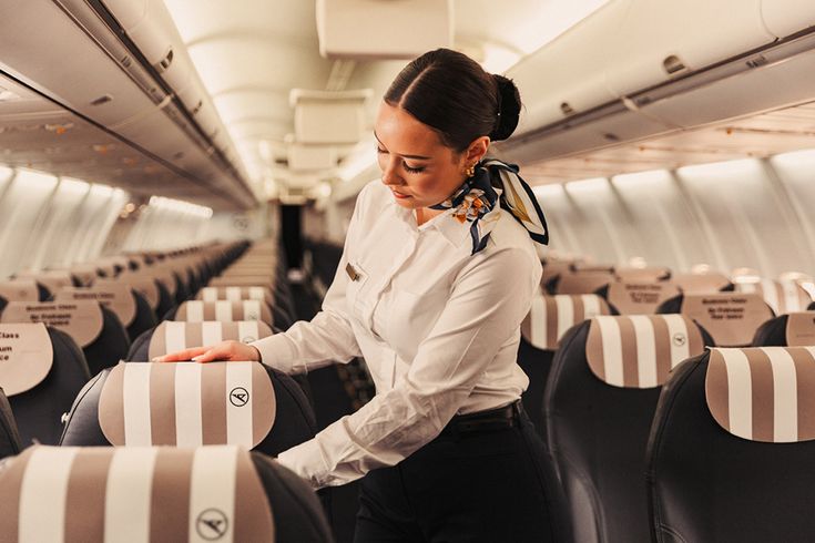 Mitglied des Kabinenpersonals richtet die Sitzplätze in der Condor Business Class her; Innenansicht einer Flugzeugkabine mit gestreiften Kopfstützenbezügen