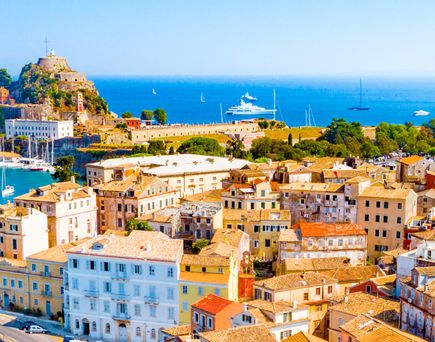 Blick auf die Küstenstadt Korfu mit dicht bebauten Häusern, einem Hafen und mehreren Booten im Meer