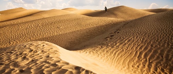 Weite Sanddünen in der Sahara mit einer einzelnen Person, die am Horizont läuft